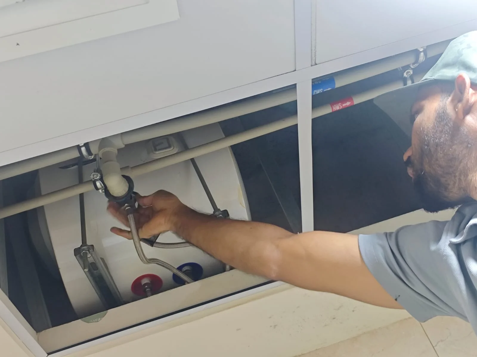 Technician repairing a water heater above a ceiling access panel in Dubai